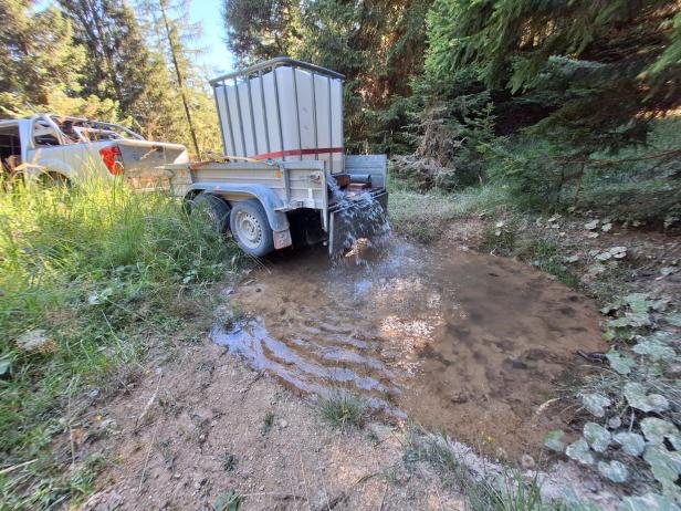 Jäger befüllt eine Wasserstelle im Wald mit einem Anhänger.