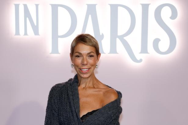 Mathilde Favier mit kurzem Haar und grauem Strickpullover lächelt vor einem Hintergrund mit der Aufschrift „IN PARIS“.