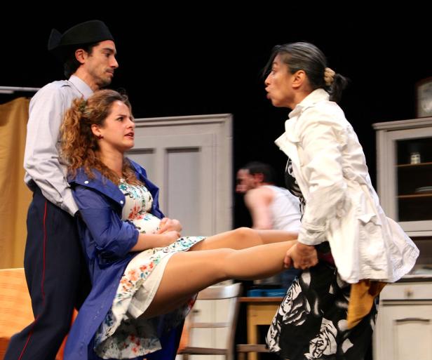 Auf einer Bühne tragen zwei Personen eine Frau in einem geblümten Kleid.