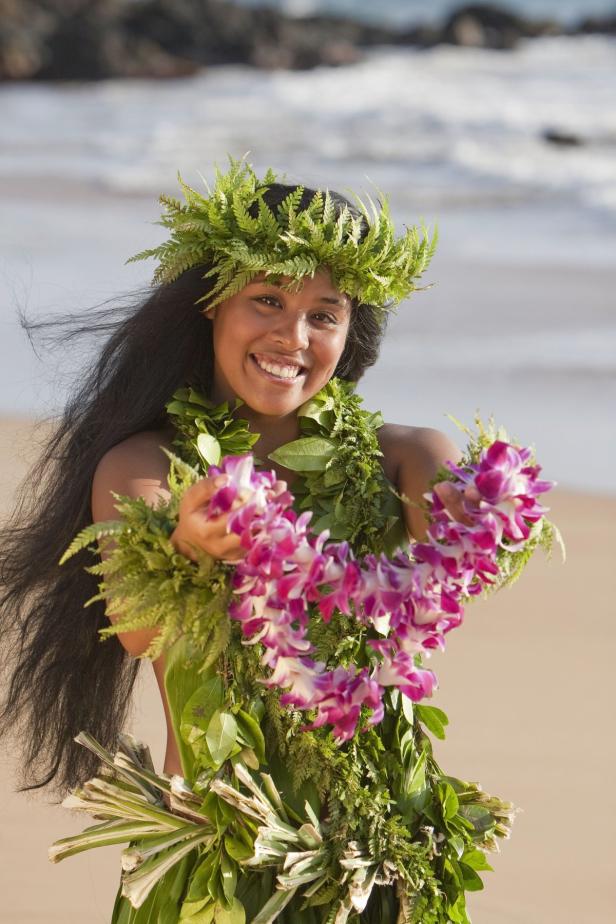 Eine lächelnde Frau mit Blumenkranz und Lei am Strand.