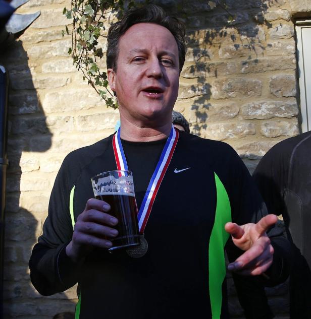 David Cameron hält ein Bier und trägt eine Medaille.