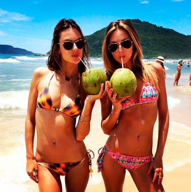 Zwei Frauen in Bikinis trinken Kokosnüsse am Strand.