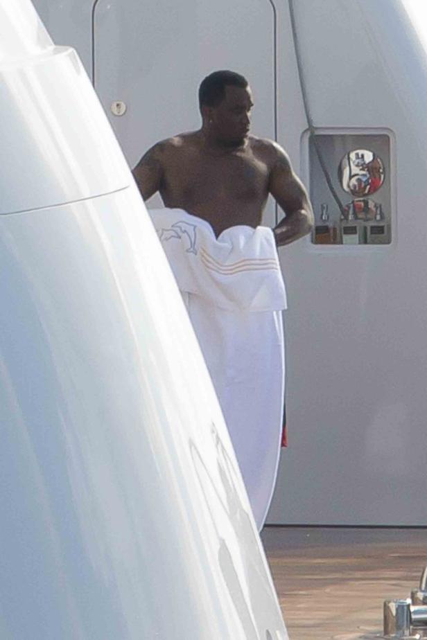 Ein Mann mit freiem Oberkörper und einem Handtuch um die Hüften steht auf einer Yacht.