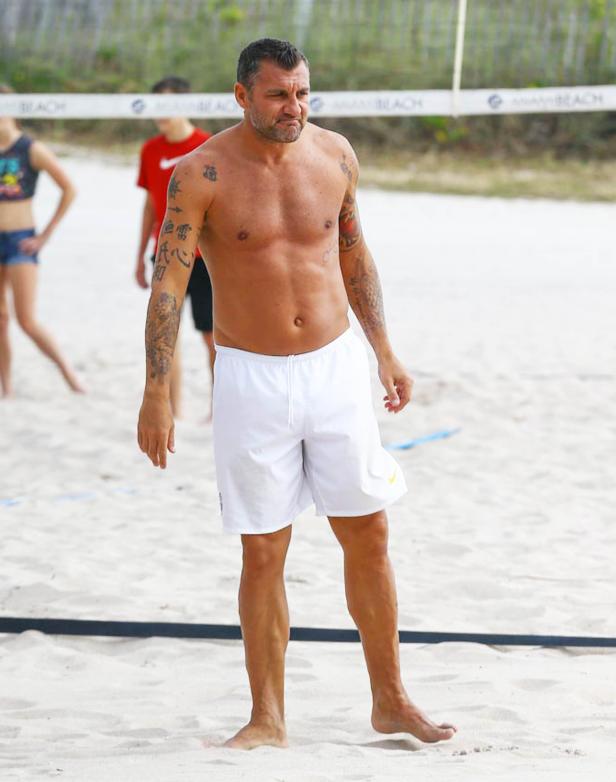 Ein tätowierter Mann steht barfuß am Strand von Miami Beach.
