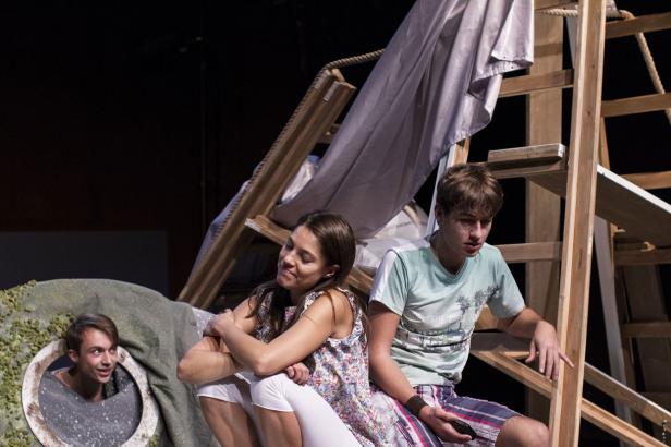 Drei junge Schauspieler auf einer Bühne mit einem Bühnenbild aus Holzleitern und einer Felswand.