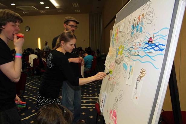 Eine Frau zeichnet auf ein Whiteboard mit Illustrationen, während andere zusehen.