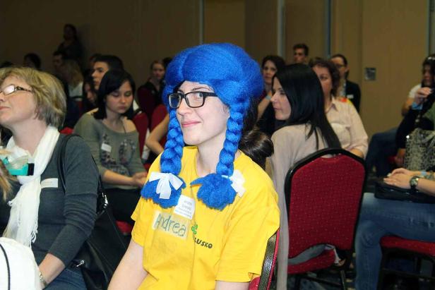 Eine Frau mit blauer Zopfperücke sitzt im Publikum.