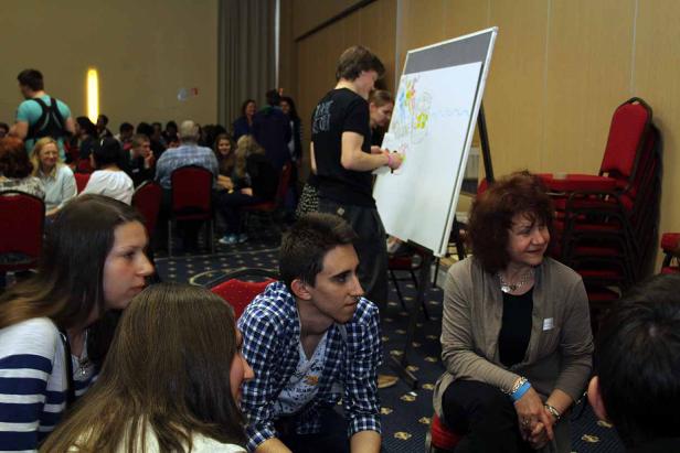 Menschen sitzen in einem Raum, während eine Person auf ein Whiteboard zeichnet.