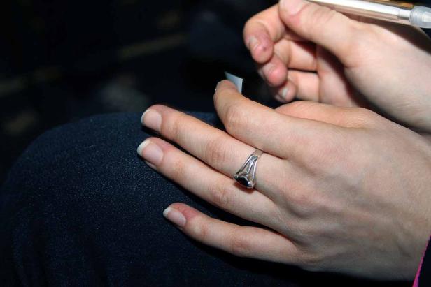 Eine Hand mit einem Ring hält einen Stift und ein kleines Stück Papier.