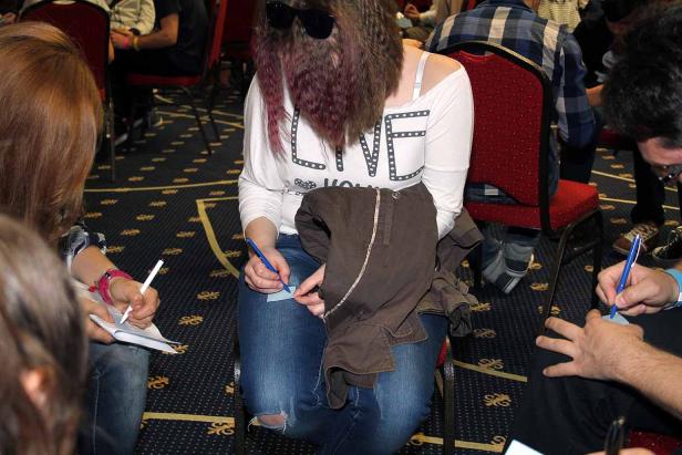 Mehrere Personen sitzen an Tischen und schreiben auf Zettel.