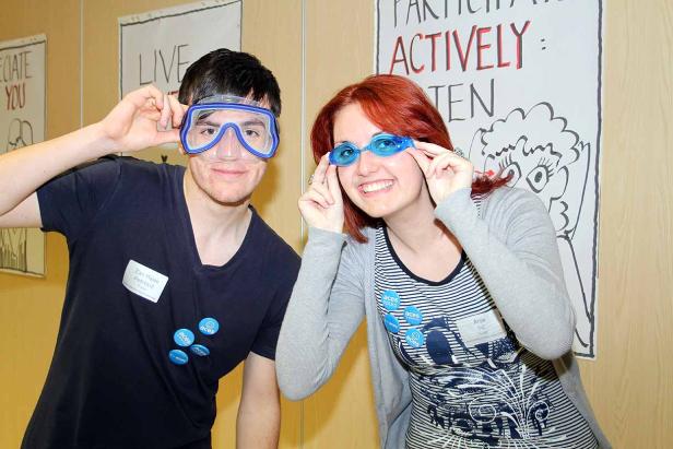 Zwei Personen posieren mit Schwimmbrillen vor einer Wand mit Aufschriften.