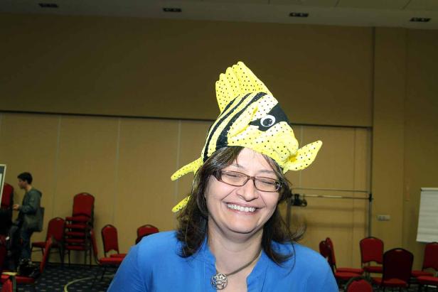 Eine lächelnde Frau trägt einen gelb-schwarz gestreiften Fischhut.