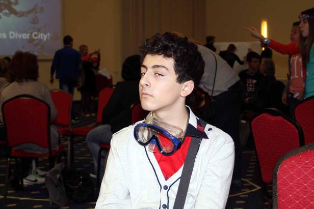 Ein junger Mann mit Taucherbrille um den Hals sitzt in einem Publikum.