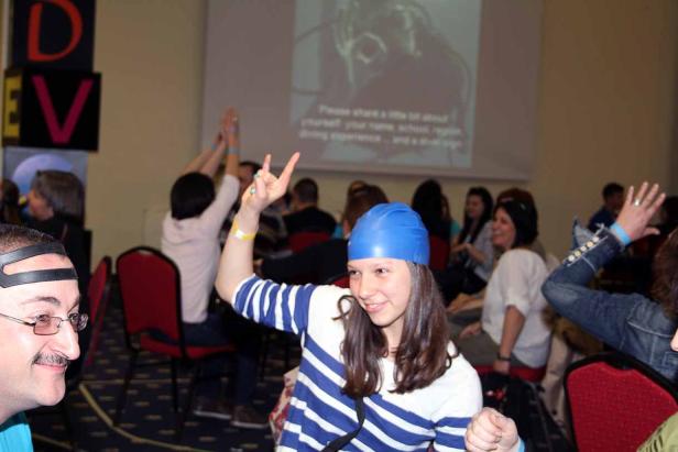 Eine junge Frau mit blauer Badekappe zeigt ein Victory-Zeichen in einem Raum voller Menschen.