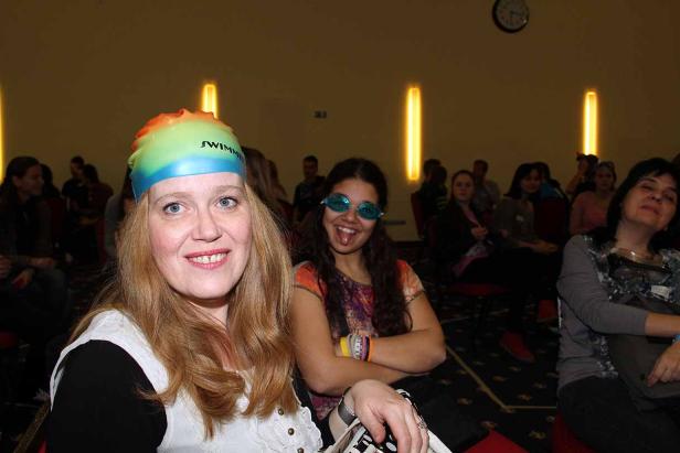 Frauen sitzen in einem Publikum, eine trägt eine Schwimmkappe, eine andere eine blaue Brille.