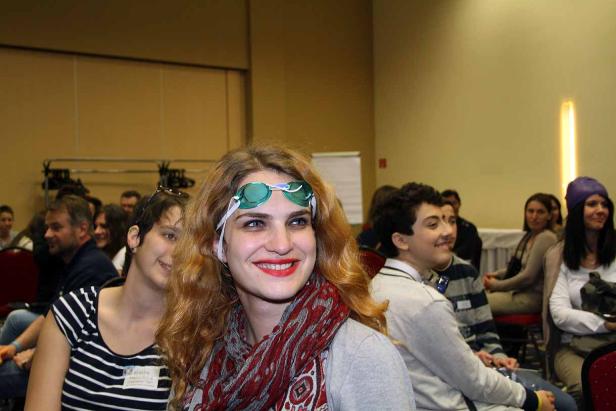 Eine lächelnde Frau mit Schwimmbrille auf der Stirn sitzt in einem Publikum.