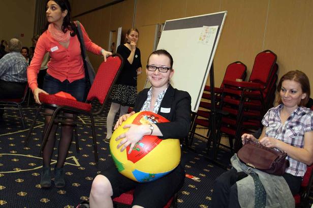 Eine Frau sitzt mit einem bunten Ball auf dem Schoß in einem Raum.