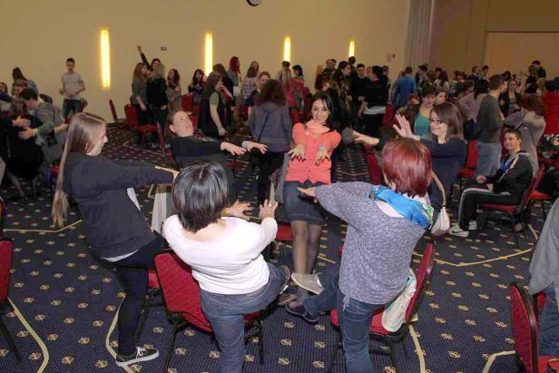 Eine Gruppe von Menschen spielt ein Spiel mit Stühlen in einem großen Raum.