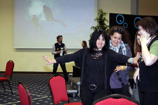 Eine Frau breitet die Arme vor einer Leinwand mit Tauchern aus, während andere Personen zusehen.