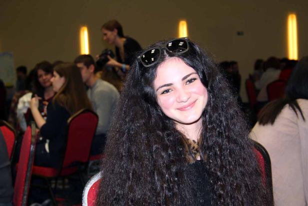 Eine lächelnde junge Frau mit Sonnenbrille auf dem Kopf in einem Raum mit anderen Menschen.