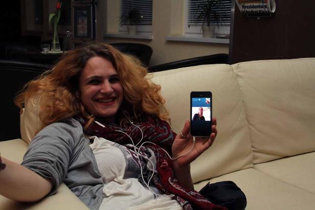 Eine Frau lächelt und hält ein Smartphone mit einem Videoanruf in der Hand.