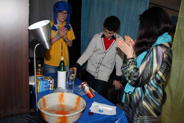 Drei Personen stehen an einem Tisch mit Requisiten und klatschen in die Hände.