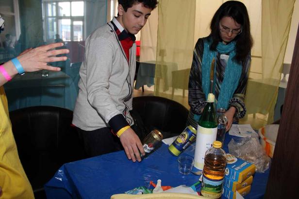 Zwei Personen stehen an einem Tisch mit verschiedenen Gegenständen, möglicherweise für ein Experiment.