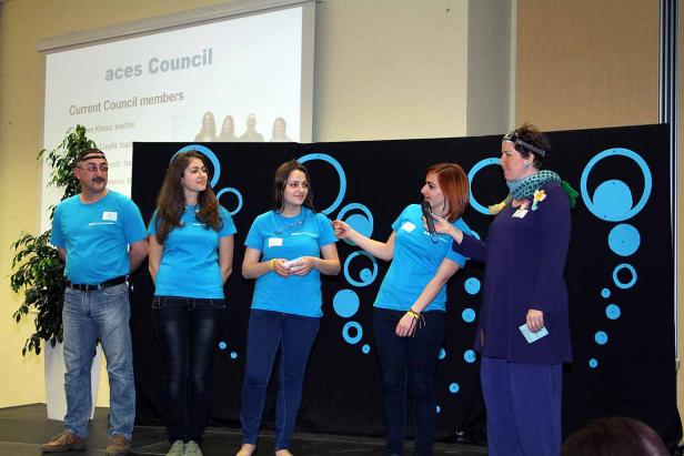Eine Gruppe von Personen steht auf einer Bühne während einer Präsentation des „aces Council“.