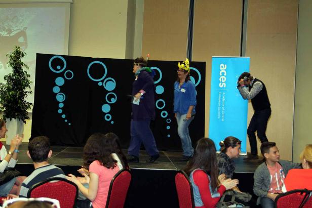 Zwei Frauen in Kostümen stehen auf einer Bühne vor Publikum.