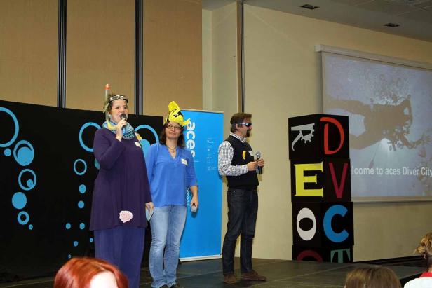 Drei Personen stehen auf einer Bühne, eine davon mit Taucherbrille und Schnorchel, eine mit einem gelben Fischhut.