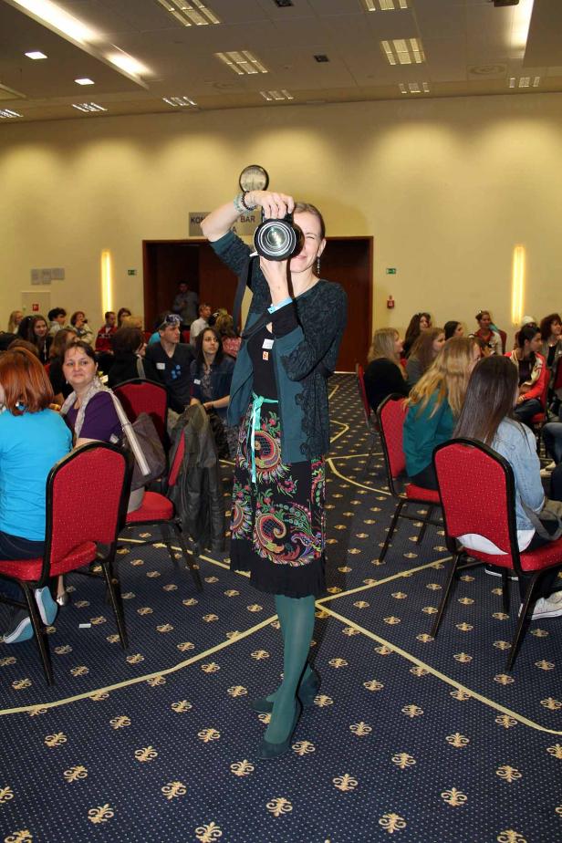 Eine Frau fotografiert mit einer Kamera in einem Raum voller Menschen.