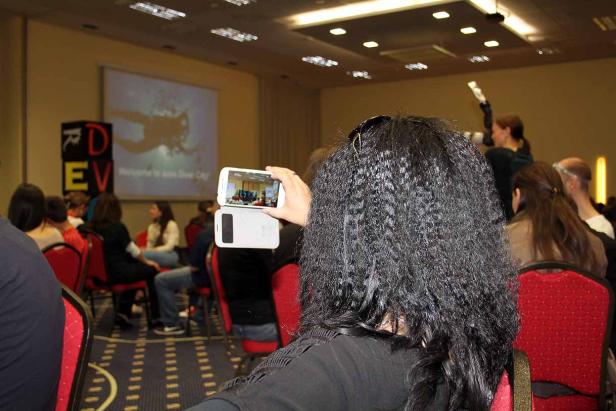 Eine Frau filmt mit ihrem Smartphone eine Präsentation während einer Konferenz.