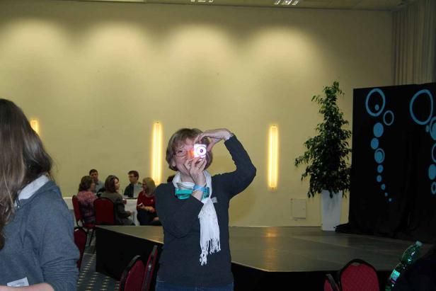 Eine Frau fotografiert mit einer leuchtenden Kamera vor einer Bühne.