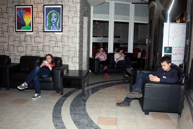 Mehrere Personen sitzen in Sesseln und Sofas in einem Wartebereich und nutzen ihre Smartphones.