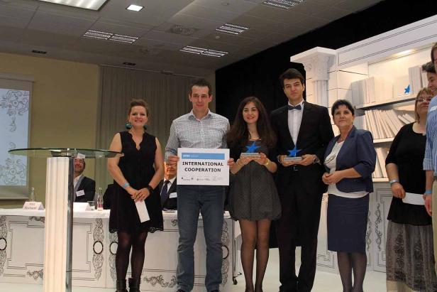 Eine Gruppe von Personen steht auf einer Bühne und hält Auszeichnungen und ein Schild mit der Aufschrift „International Cooperation“.