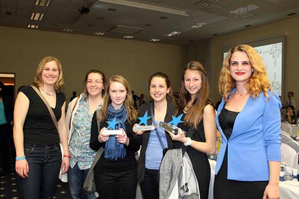 Eine Gruppe junger Frauen posiert mit blauen Stern-Trophäen für ein Foto.