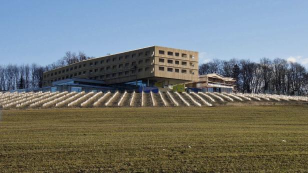 Ein großes, modernes Gebäude auf einem Hügel mit neu gepflanzten Bäumen im Vordergrund.