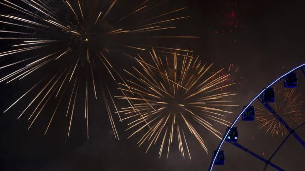 Feuerwerk erhellt den Nachthimmel neben einem beleuchteten Riesenrad.