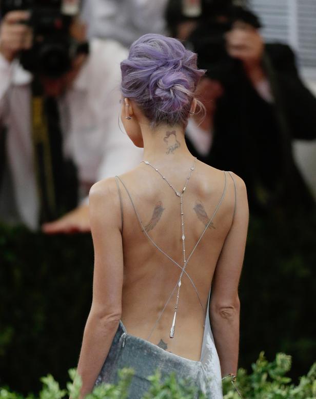 Eine Frau mit lila Haaren und Tätowierungen auf dem Rücken trägt ein rückenfreies Kleid.