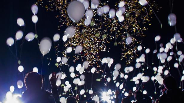 Menschen feiern mit weißen Ballons und Konfetti in der Luft.