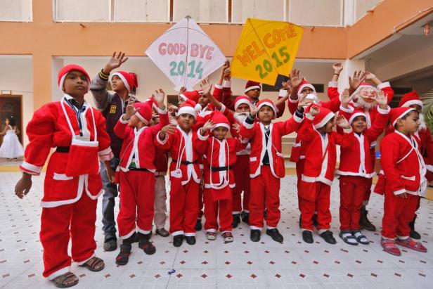 Eine Gruppe Kinder in Weihnachtsmannkostümen hält Schilder mit „Goodbye 2014“ und „Welcome 2015“.