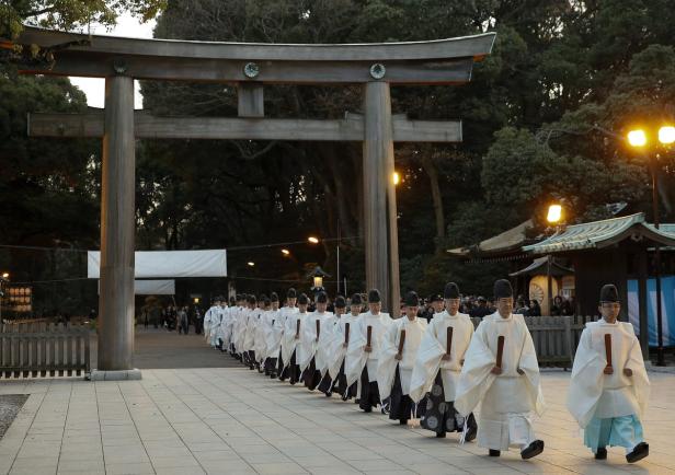 Eine Prozession von Shinto-Priestern schreitet durch ein Torii-Tor.