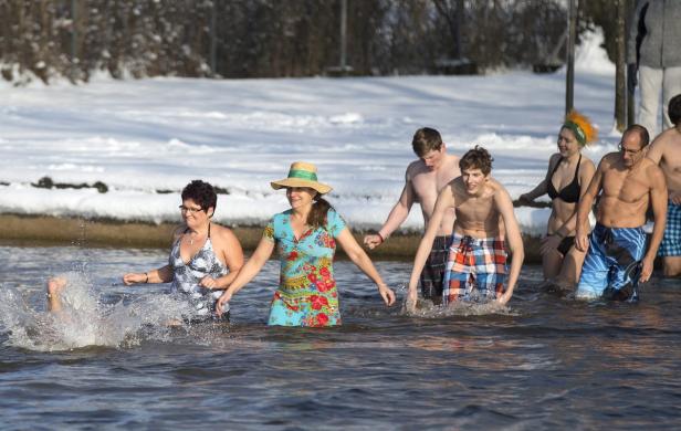 Eine Gruppe Menschen watet im Winter in einem See.
