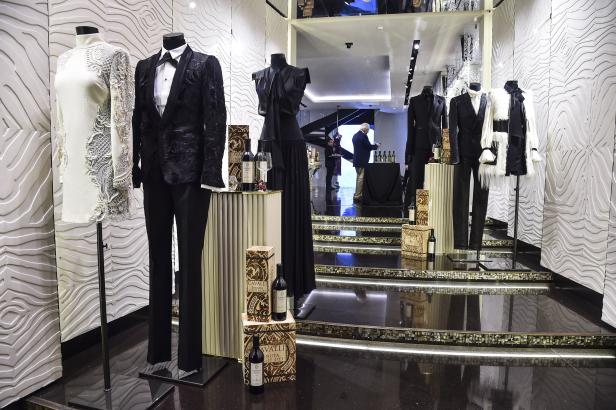 Ein Schaufenster mit eleganten Kleidern und Anzügen, dekoriert mit Weinflaschen der Marke Cavalli.
