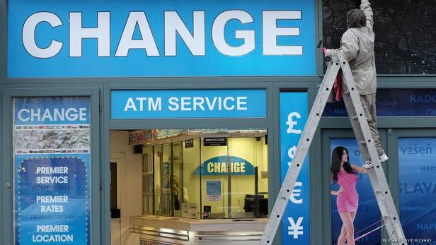 Ein Mann streicht das Schild einer Wechselstube, auf dem auch eine Werbung zu sehen ist.