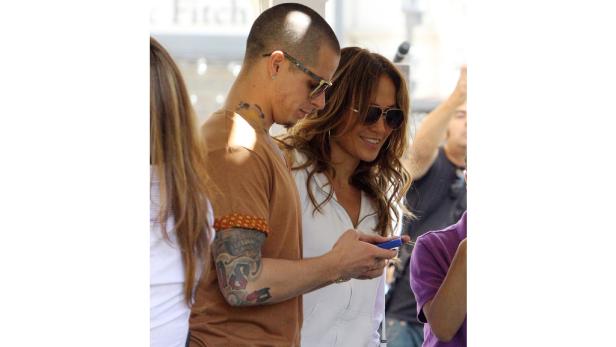 Jennifer Lopez und ein Mann mit Tattoos schauen auf ein Handy.