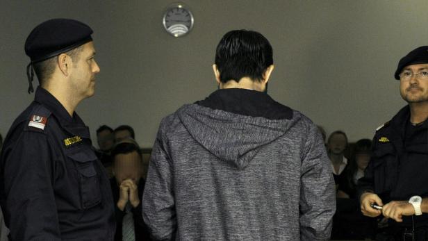 Ein Mann mit dem Rücken zum Betrachter, flankiert von zwei Justizbeamten.