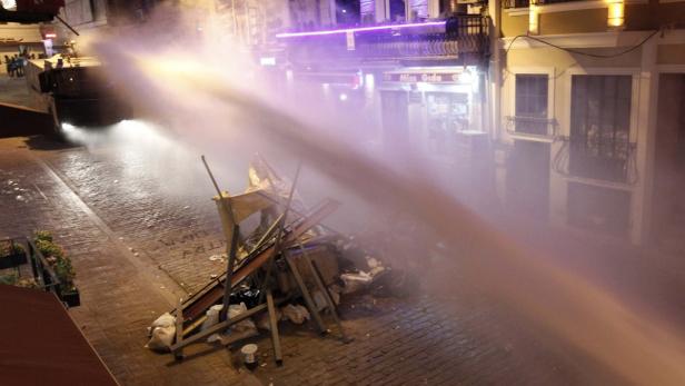 Ein Wasserwerfer wird gegen eine Barrikade auf einer Straße eingesetzt.