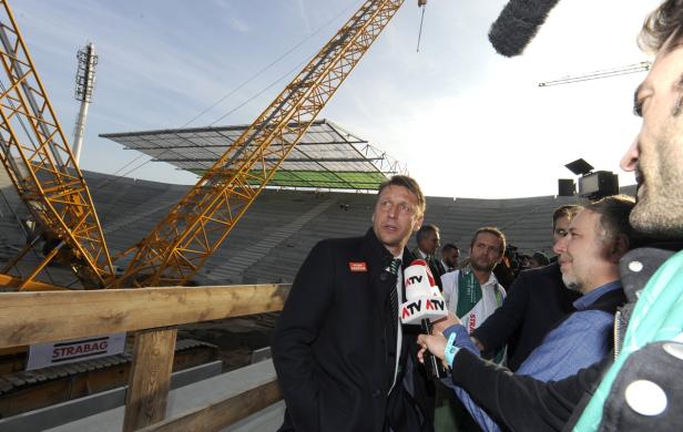 Ein Mann wird vor dem Hintergrund des Stadionbaus interviewt.