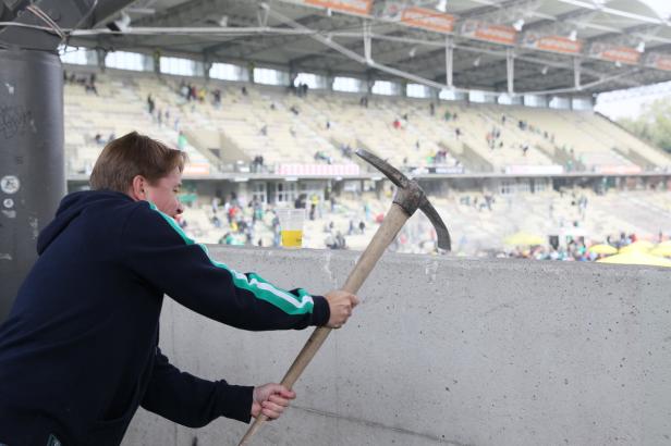 Ein Mann hält eine Spitzhacke vor einem Fußballstadion.